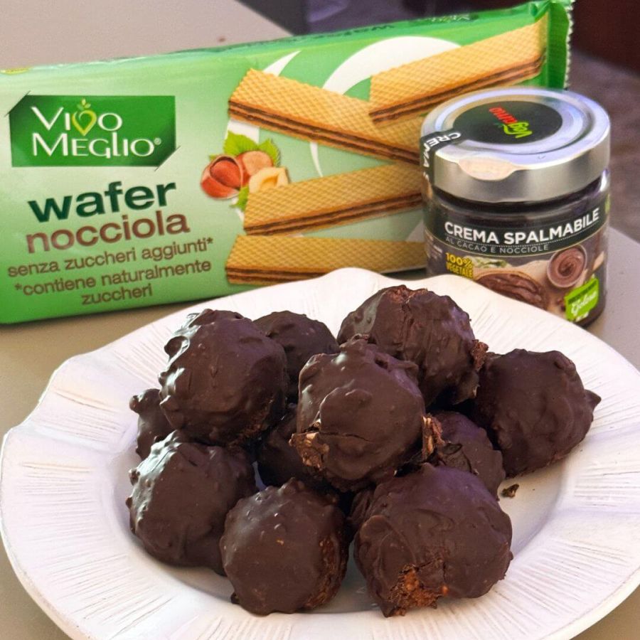 Tartufini vegani stile Rocher con nocciole e cioccolato fondente, senza glutine, serviti su un piatto con granella croccante.