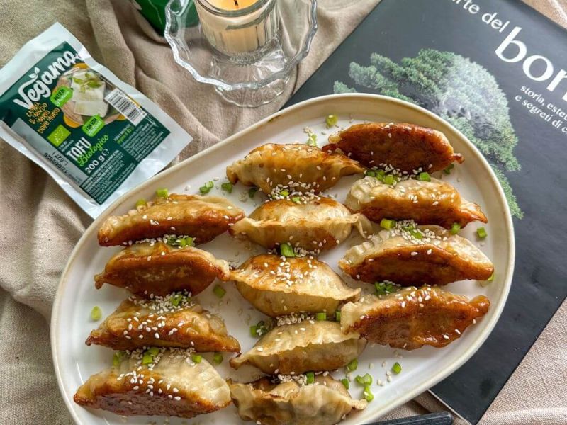 Gyoza vegetariani dorati cotti in padella con ripieno di tofu Vegamo e verdure, guarniti con semi di sesamo e cipollotto fresco.