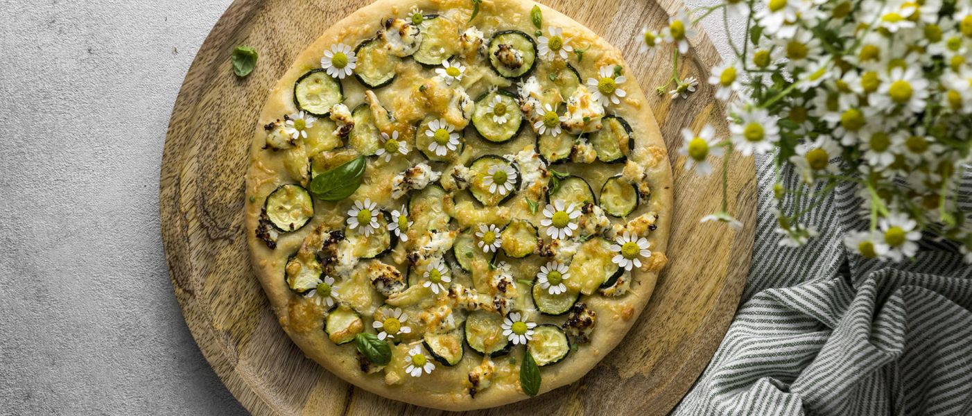 Pizza vegetariana con zucchine, formaggio fuso, basilico e fiori commestibili su tagliere di legno