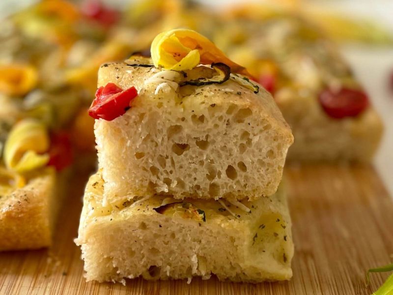 Focaccia proteica con tofu, zucchine, pomodorini rossi e gialli, fiori di zucca e condimenti aromatici, piatto vegano e ricco di proteine