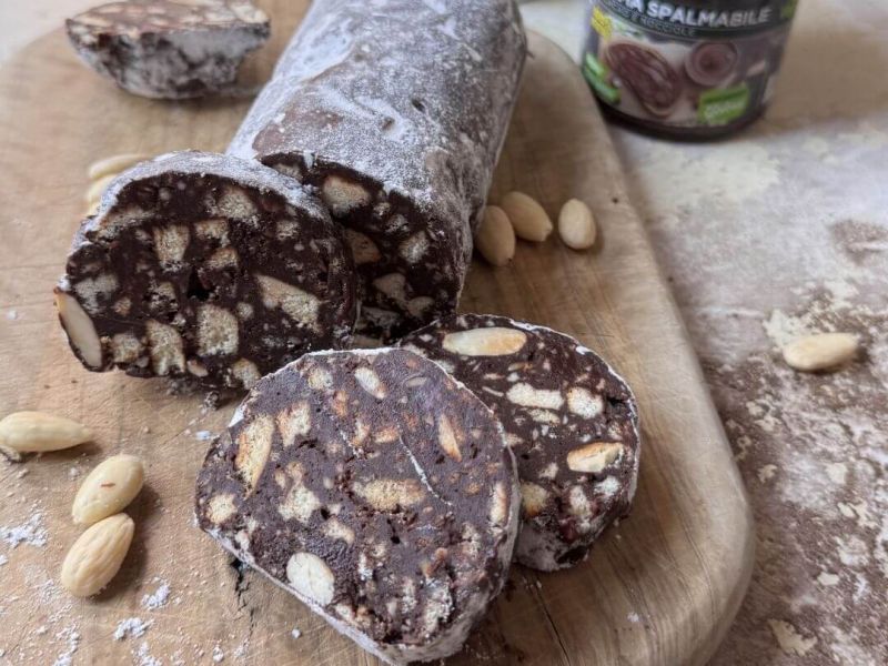 Salame di cioccolato vegano tagliato a fettine, decorato con zucchero a velo, pronto da servire come dolce facile e goloso