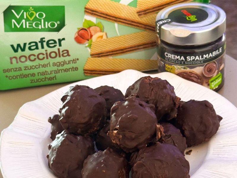 Tartufini vegani stile Rocher con nocciole e cioccolato fondente, senza glutine, serviti su un piatto con granella croccante.